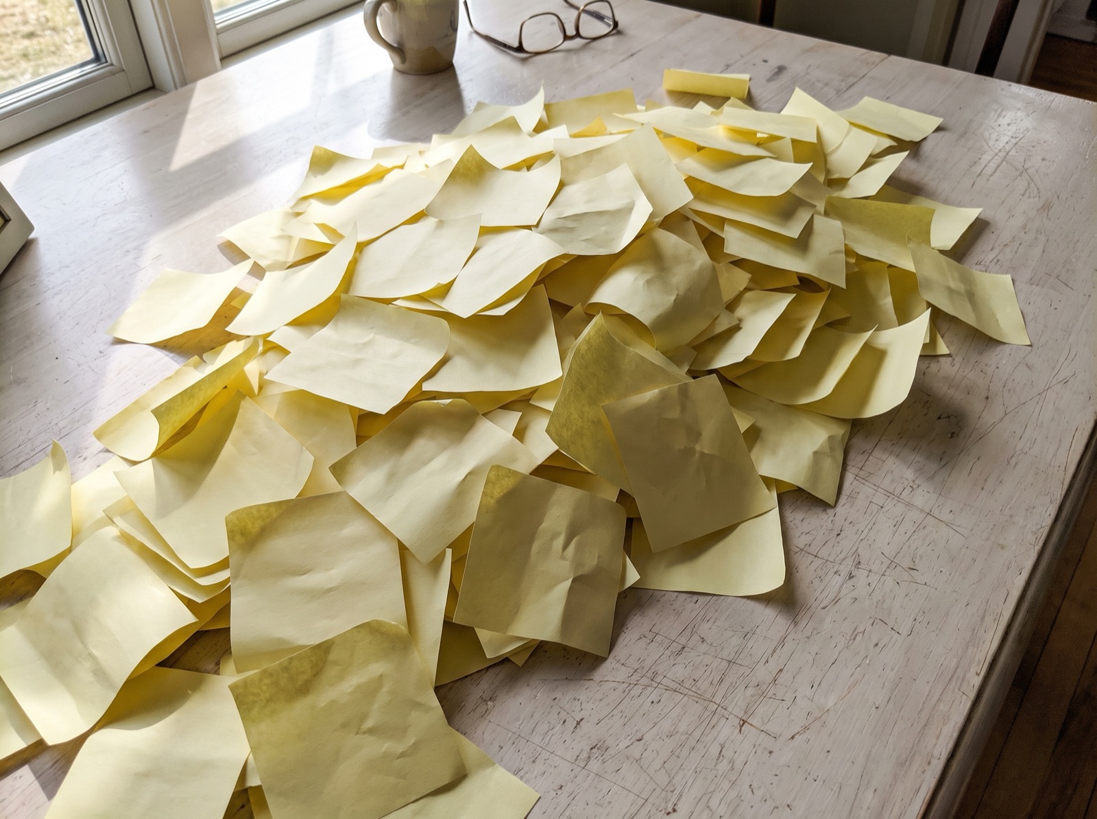 A heap of blank yellow sticky notes spilling across a light wooden table in daylight