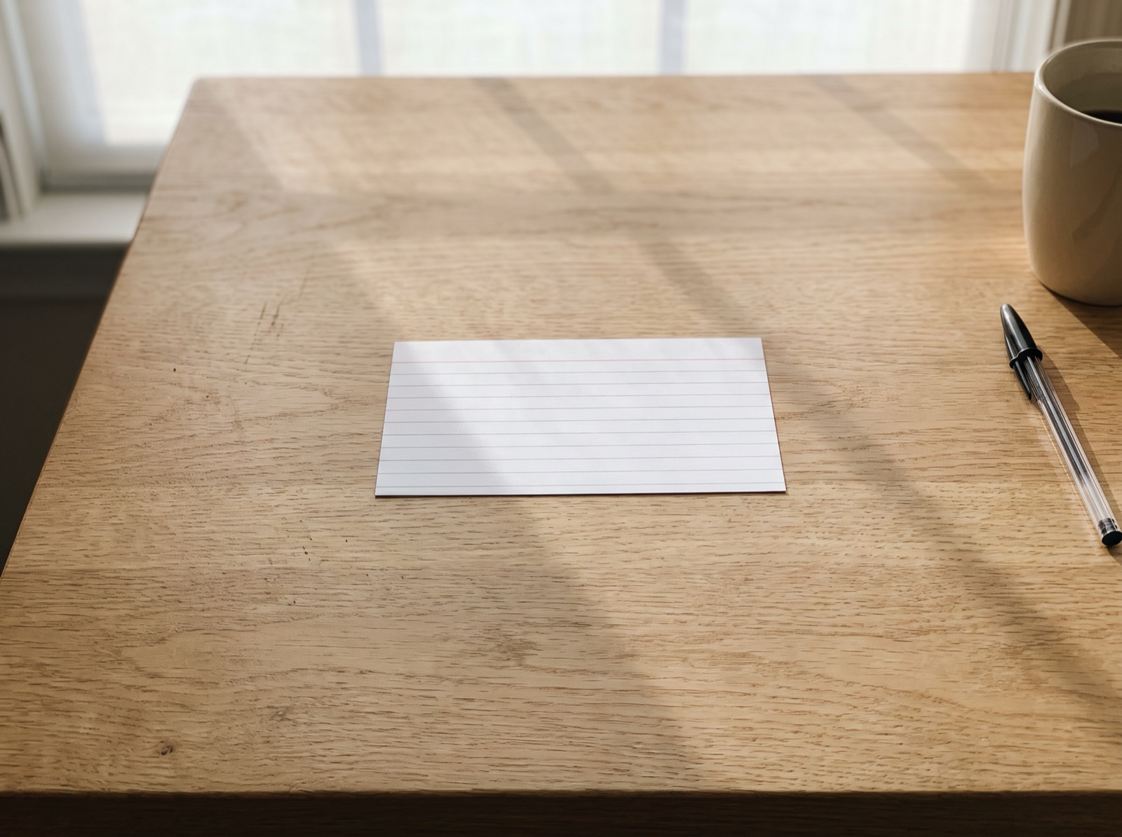 A single blank index card lying on an otherwise empty light oak desk in morning light
