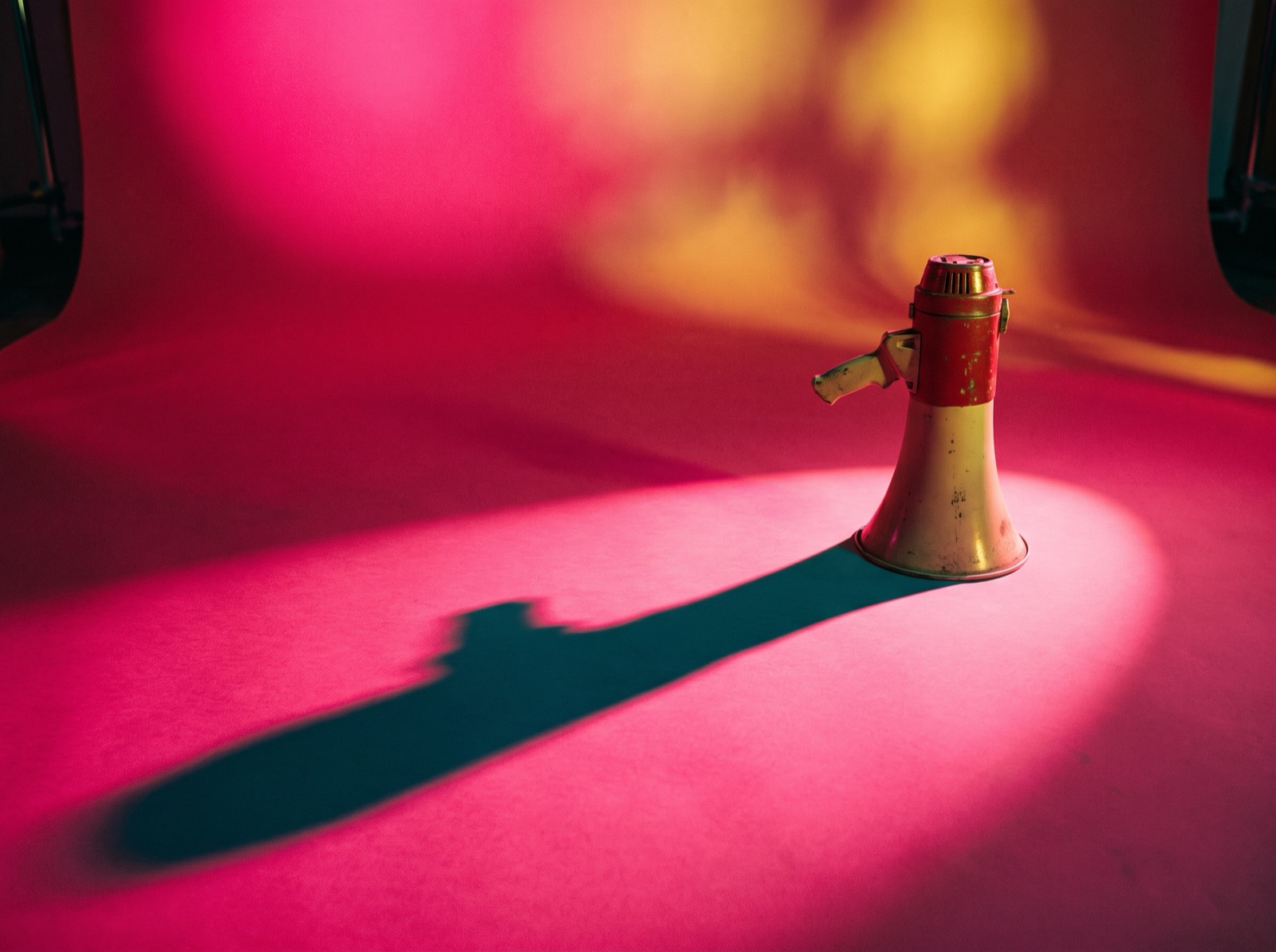 A small megaphone casting a giant shadow on a pink backdrop