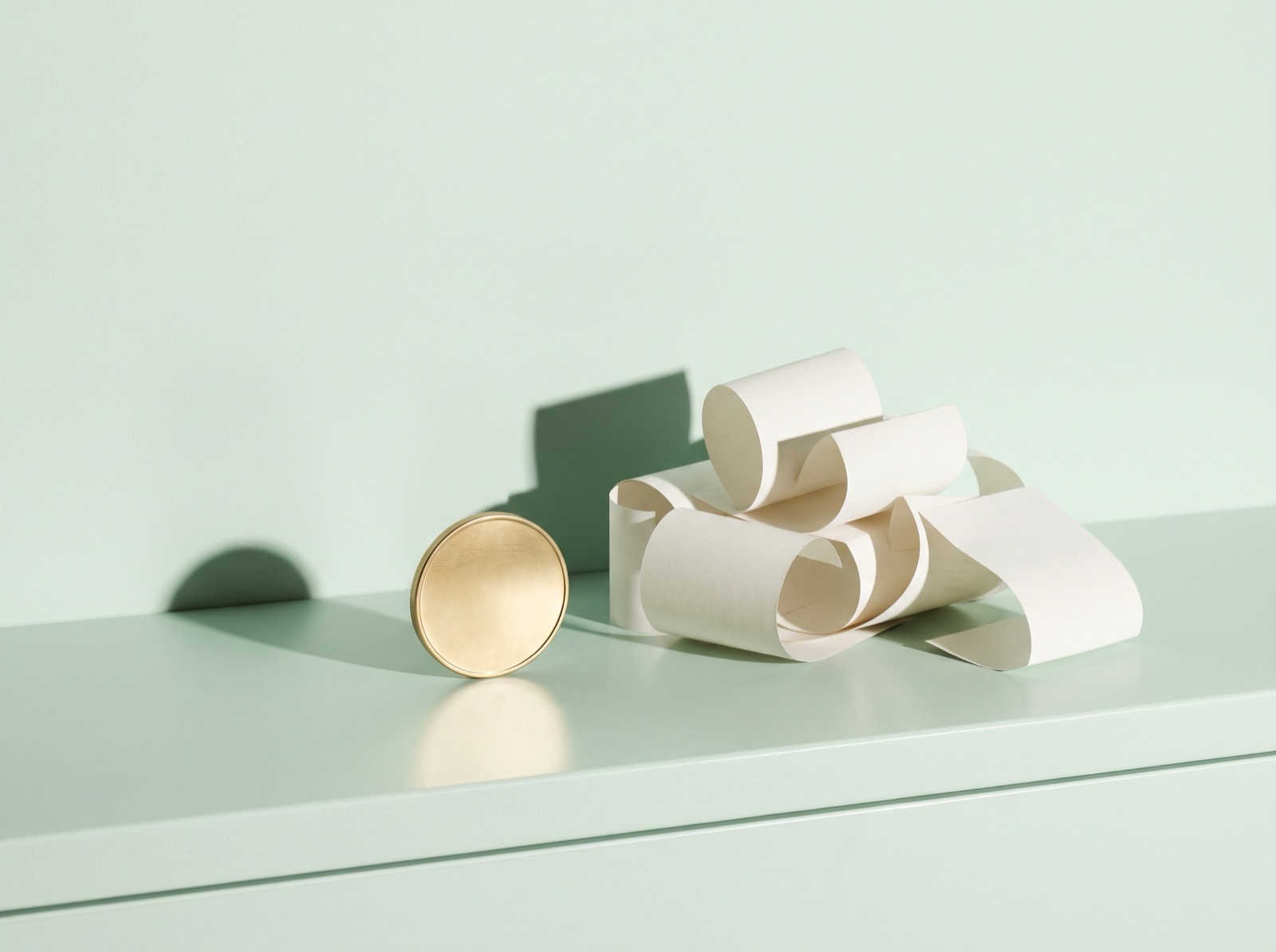 A plain gold coin standing on its edge beside a heap of curling blank paper receipts on a mint-green counter