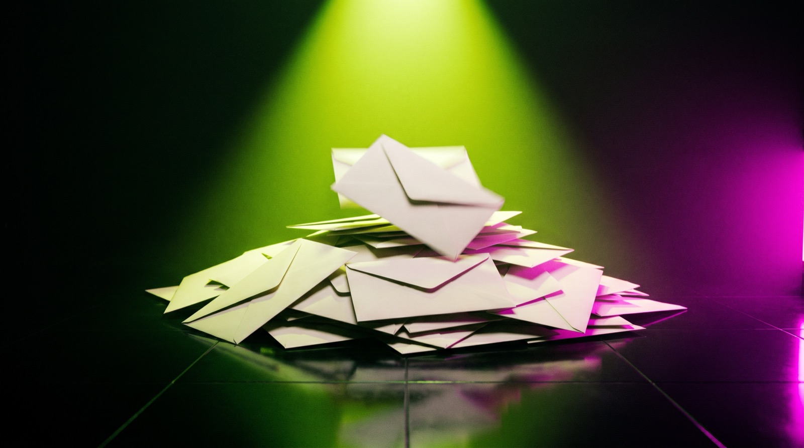 A heap of sealed blank envelopes on a glossy black floor under an acid-lime spotlight, lit magenta at one edge